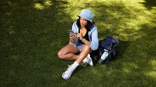 Woman using her phone while outside, in a field or park.