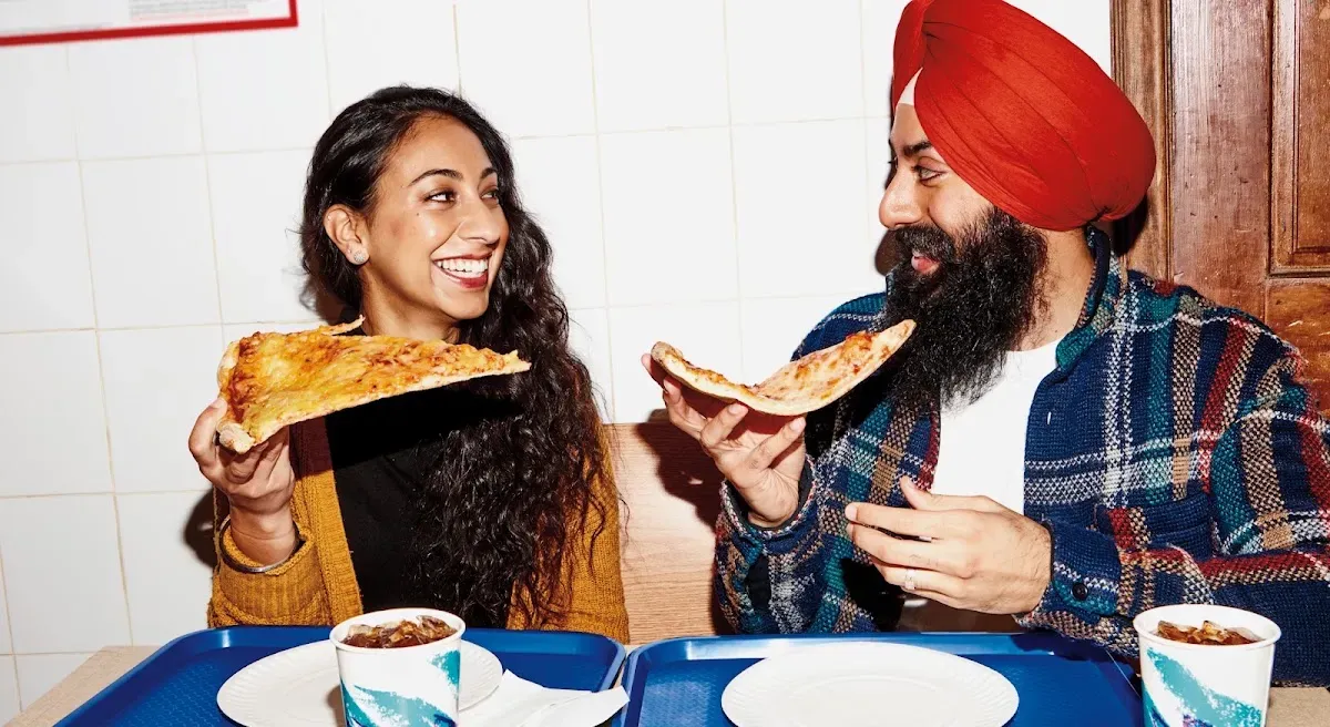 a woman and a man smile at each other while eating slices of pizza
