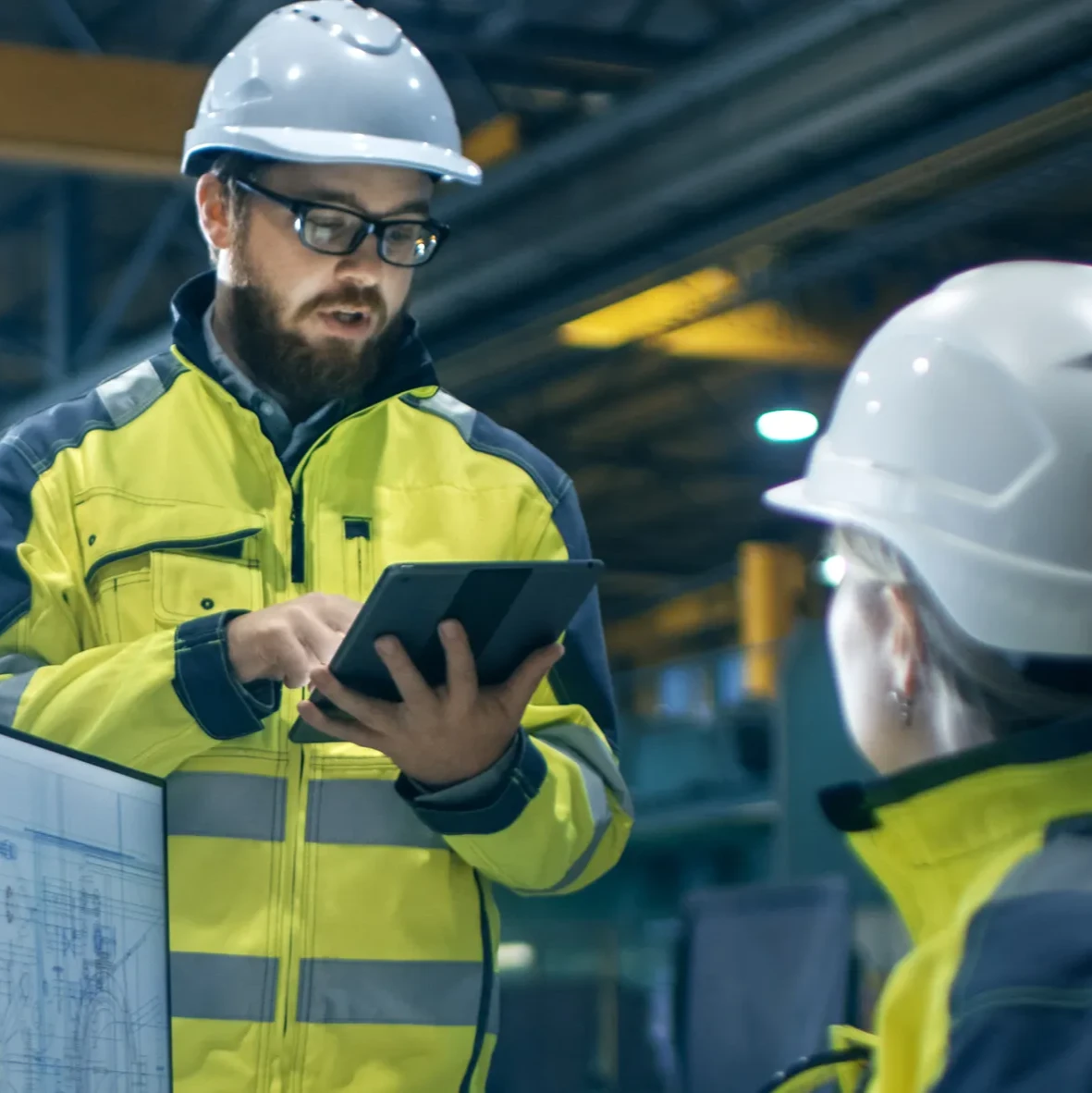 Workers in yellow vests and white hard hats using a computer