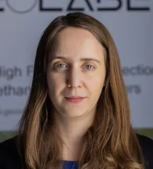 A professional portrait of a woman with long light brown hair in front of a GeoLabe banner, representing a New Mexico-based company using AI and satellites to monitor environmental threats.