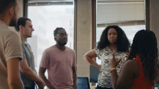 five people standing in a circle talking, two backs are to the camera