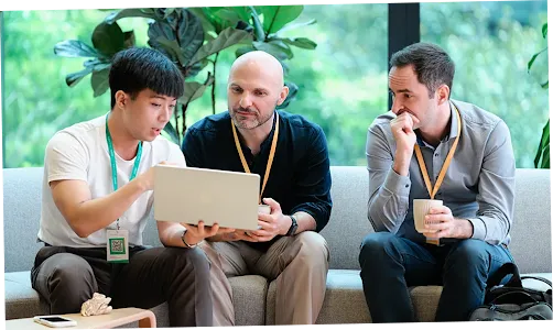Three people: one is holding a coffee mug while the other two look at a laptop.