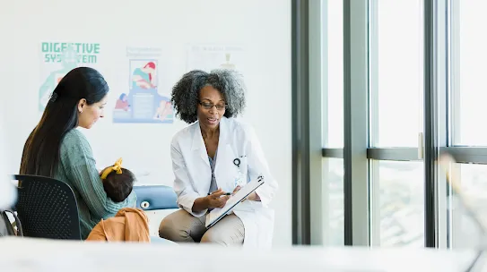 A female doctor in a white coat shows a woman with a baby a medical chart