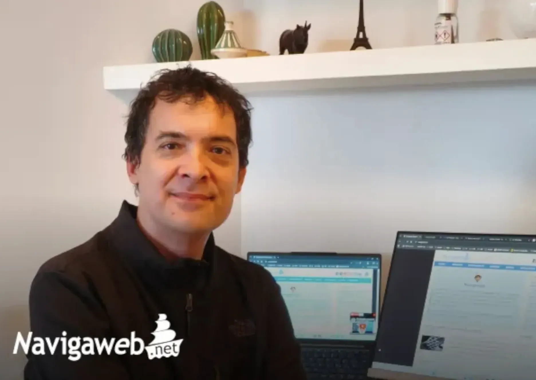 Image of a man wearing a black shirt sitting in front of a computer looking at the camera