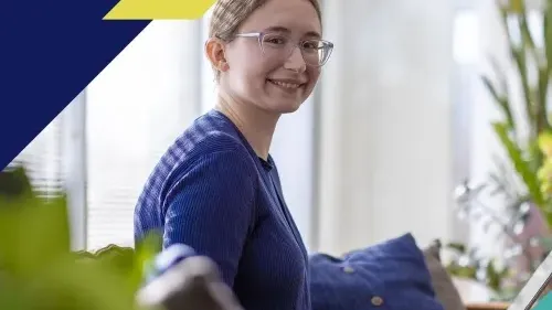 A young woman with glasses and a blue sweater sits on a sofa, smiling while working on a laptop. The image features modern graphic design overlays in navy blue, lime yellow, and teal in the corners. It is used to represent the Google and Ipsos "AI Works for America" poll findings.