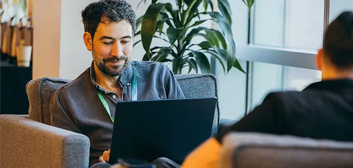 Man working on a laptop while talking to a colleague.