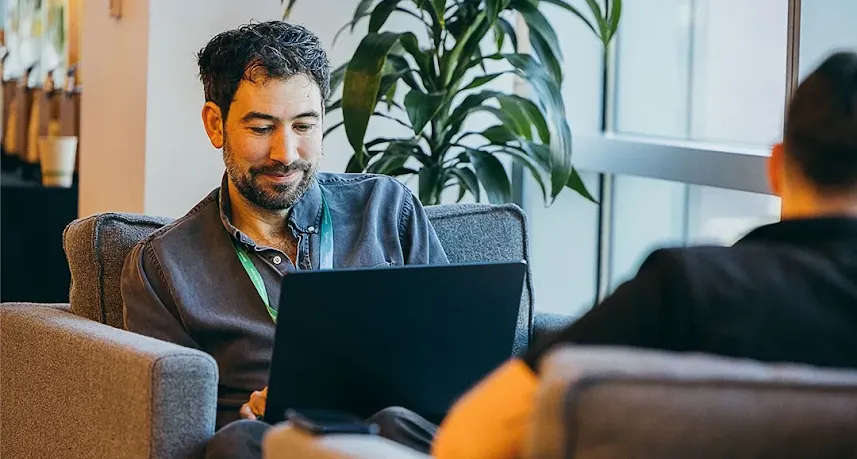 Man working on a laptop while talking to a colleague.