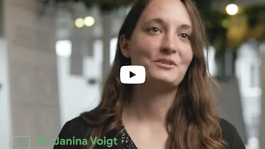 A portrait of Dr. Janina Voigt, Engineering Manager at the Google Safety Engineering Center (GSEC) in Munich. She is speaking with a friendly expression in a bright, modern office environment. A green and white lower-third graphic identifies her name and role, and a white YouTube play button is centered over the image.