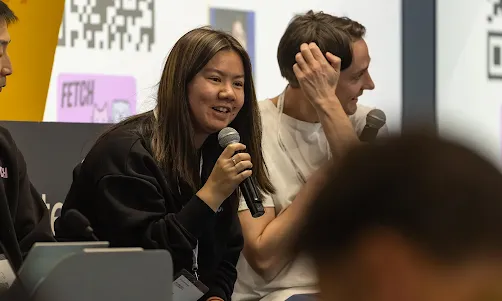 One of the event hosts, holding a mic, is speaking to the audience.