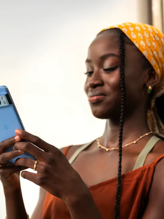 A woman with yellow patterned headscarf smiling while using a blue Google Pixel smartphone to send a message.