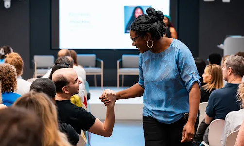 A female host shakes the hand of an audience member.