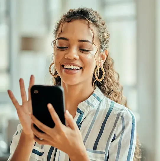 A Black female office employee wearing golden earrings and a striped button up shirt smiling while using a corporate mobile device.