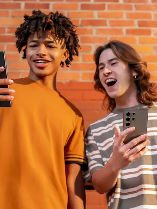Dois homens jovens segurando smartphones. O homem da direita está observando algo na tela do outro.