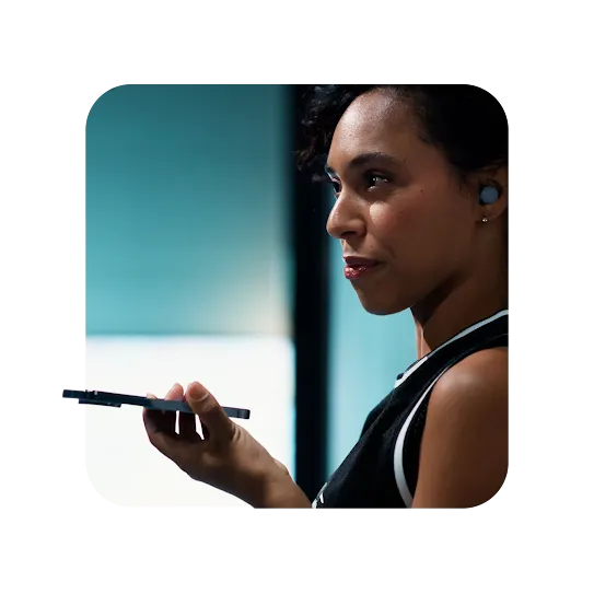 Woman wearing earbuds and looking at her phone.