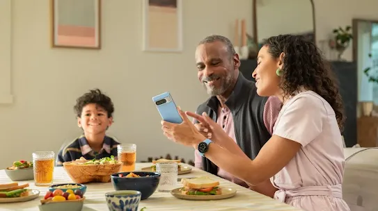 A family enjoying a meal together. The woman depicted shows something on her Android device to the man.
