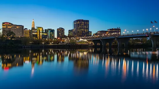 View of a downtown cityscape at dusk with lights shining off of a waterway
