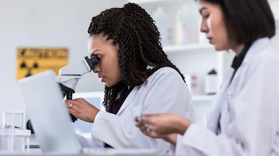 Scientist working in a lab wearing a white coat and looking into a microscope