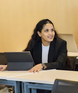 A woman wore black suit who seated on a bench and looking at something.