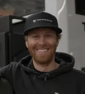 A smiling man with a beard wearing a black Truckhouse branded baseball cap and hoodie, featured in a Nevada case study about using AI to build expedition vehicles.