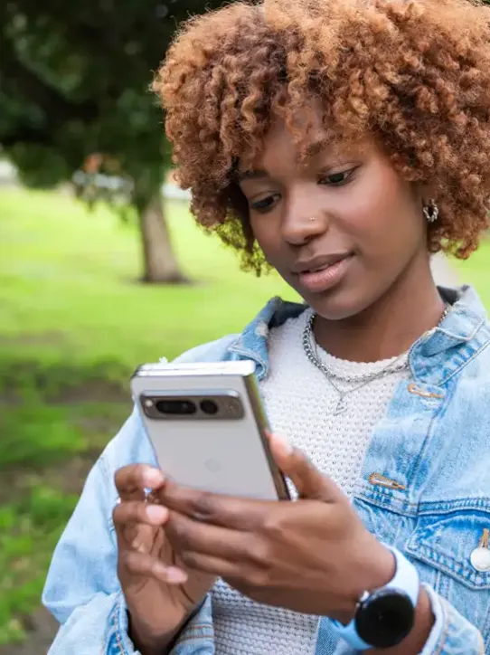 A woman in a park holding a smartphone.