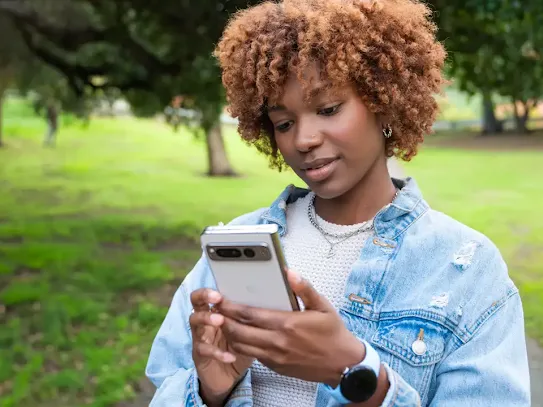 Une femme debout dans un parc, regardant son téléphone Android
