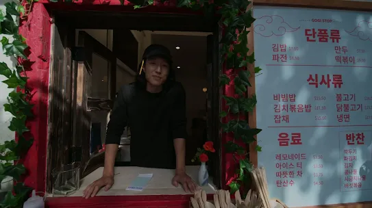 A view of a friendly person in a food stall window with an overlay that says ‘Translate Korean’. Another overlay appears with a greeting translated into English. 