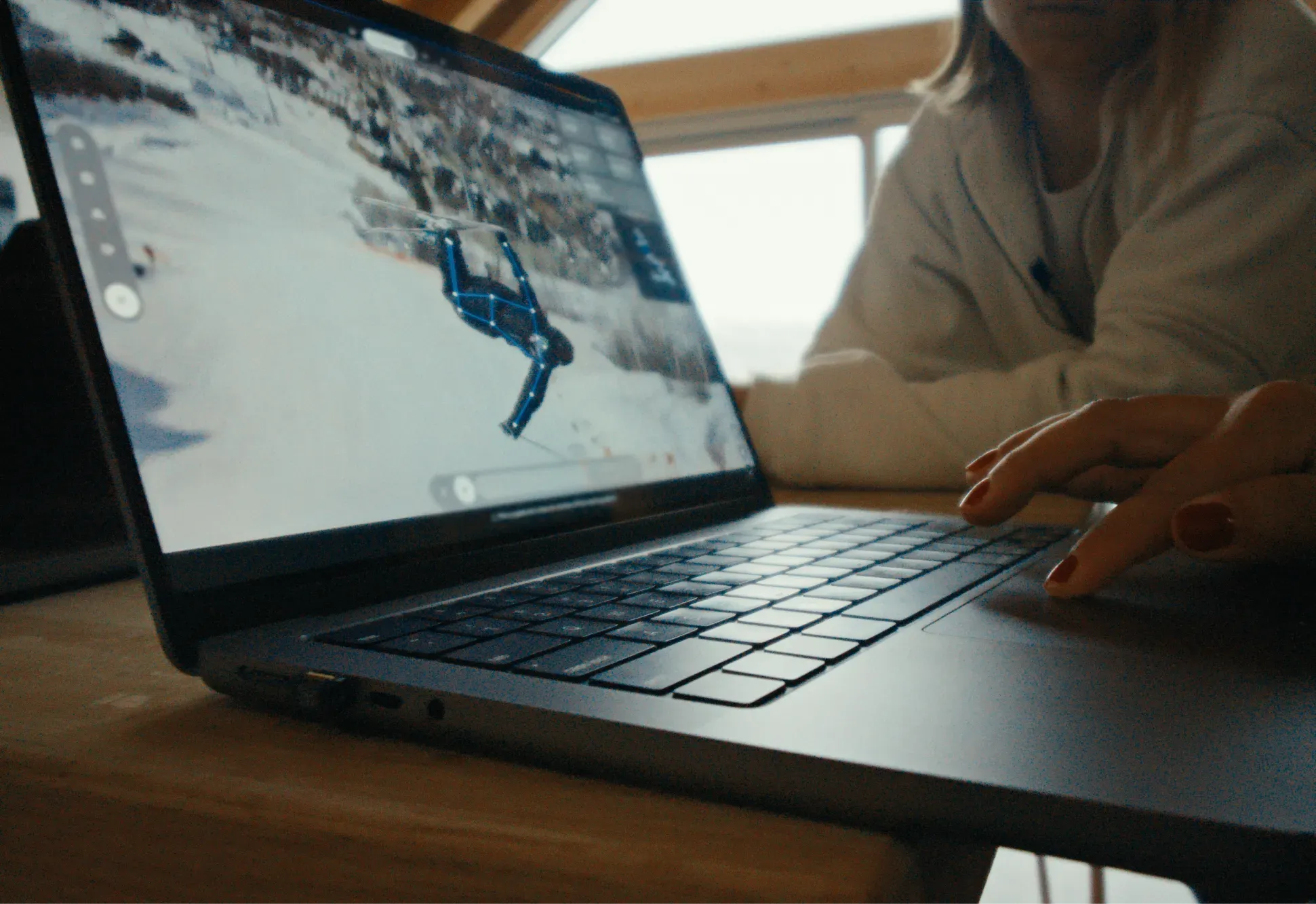 A laptop shows a skier performing a trick in mid-air on a snow-covered slope, with a video analysis tool overlaid on the image to track the athlete's movement and position.