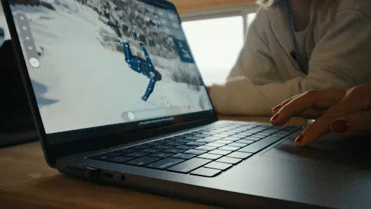 A laptop shows a skier performing a trick in mid-air on a snow-covered slope, with a video analysis tool overlaid on the image to track the athlete's movement and position.