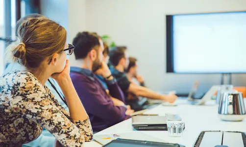 A woman wearing blue top in focus talking to another woman facing away from the camera.