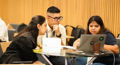 Three team members collaborating and reviewing data on a laptop screen.