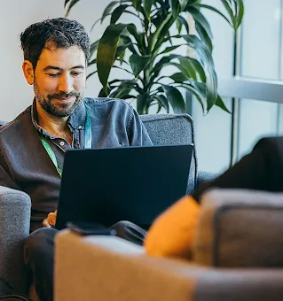 Man working on a laptop while talking to a colleague.