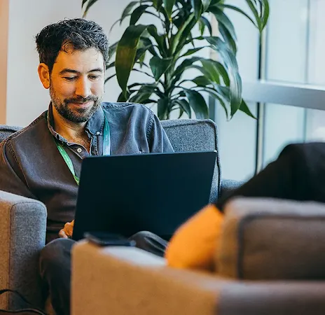 Man working on a laptop while talking to a colleague.