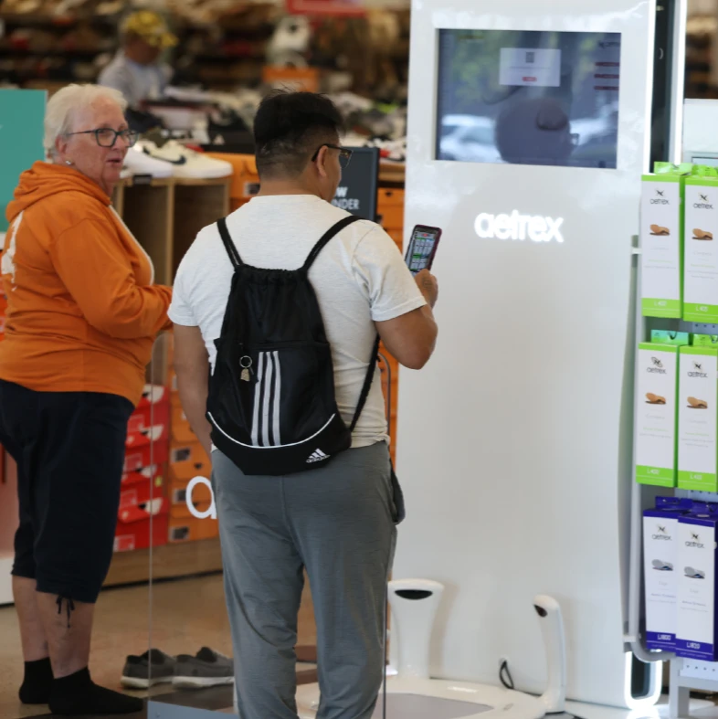 Two customers use an information kiosk in a store with their smartphones in hand