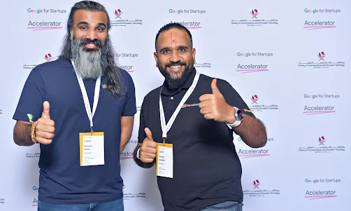 Two people wearing ID badges are posing for a photo in front of the event banner.