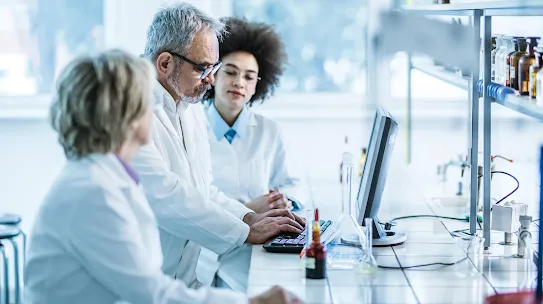 Three scientists in white lab coats collaborating in a laboratory setting