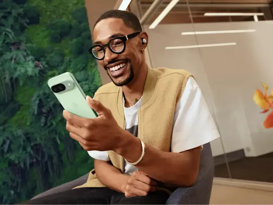 Man is sitting down in a chair and smiling while looking at his Pixel 9 phone.