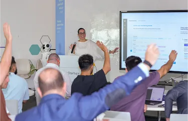 In a happy setting, the host is presenting, and attendees are raising their hands, ready to answer.