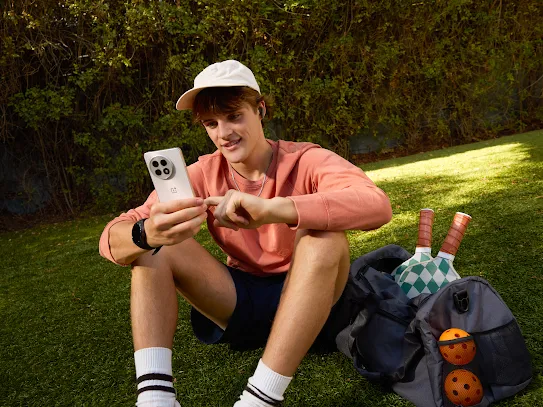 A young man using an Android phone on a grassy field.