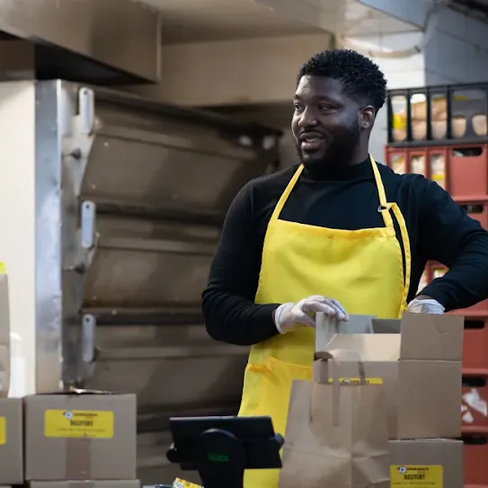 A man loads baked goods into cardboard boxes in an industrial kitchen, ready for delivery.