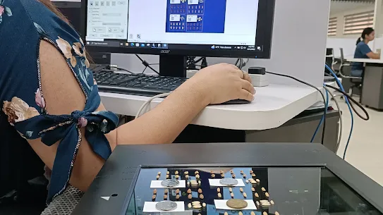 A researcher wearing a pink face mask uses a high-resolution scanner and computer software to digitize and analyze individual rice grains. Coins are placed on the scanner bed for scale during the imaging process.