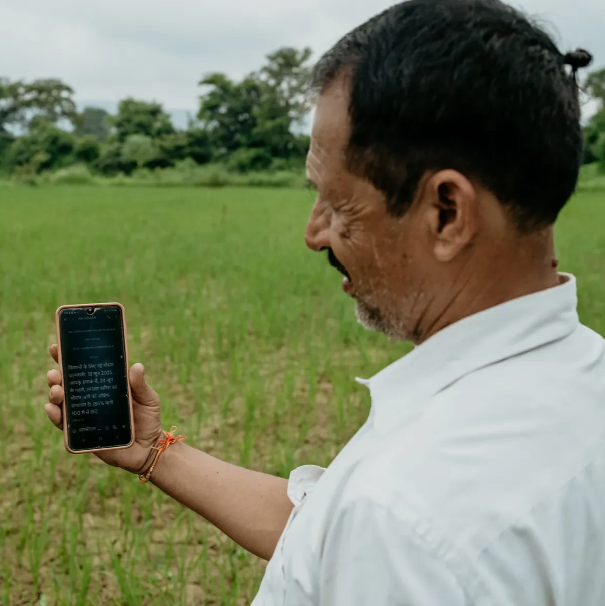 Farmer standing in a field looking at a smartphone screen with text on it.