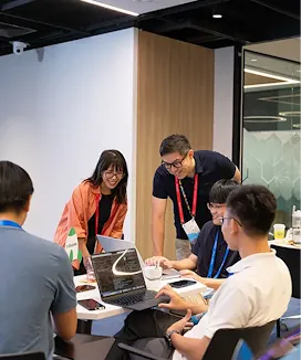 A conference room meeting where two people stand behind the host to view his laptop.