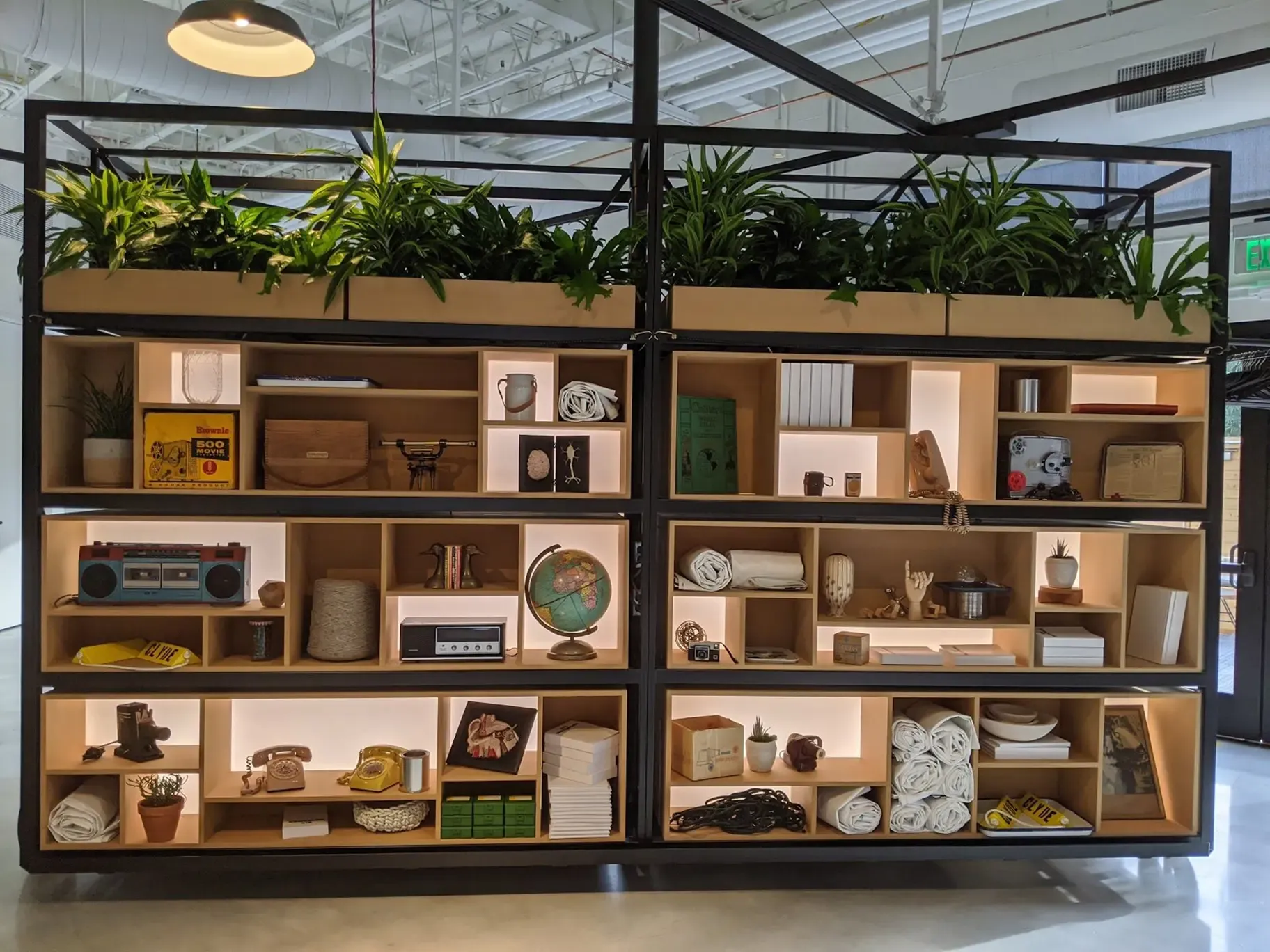 A bookshelf with various knick knacks and plants. 