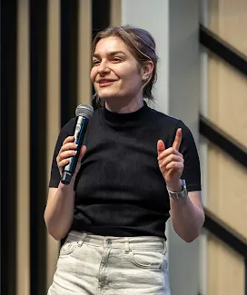 A lady is addressing a large event audience with a mic.