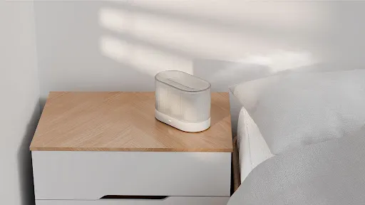 A diffuser device shown on a bedside table next to a bed