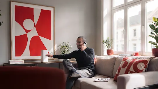 A male talks talks on the phone while sitting on a cozy, modern living room.