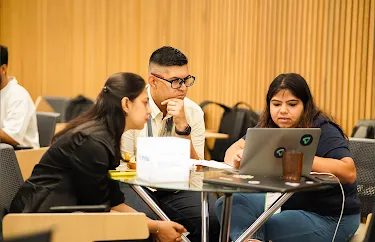 Three team members collaborating and reviewing data on a laptop screen.