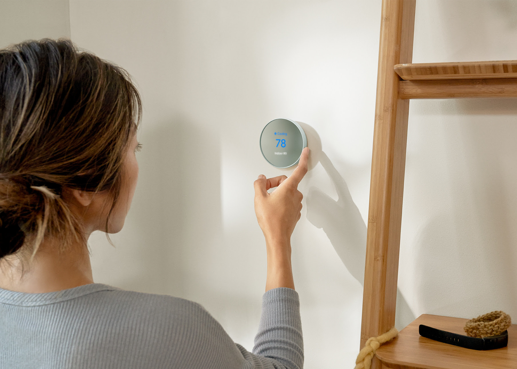 A woman is seen adjusting the temperature of a Nest thermostat