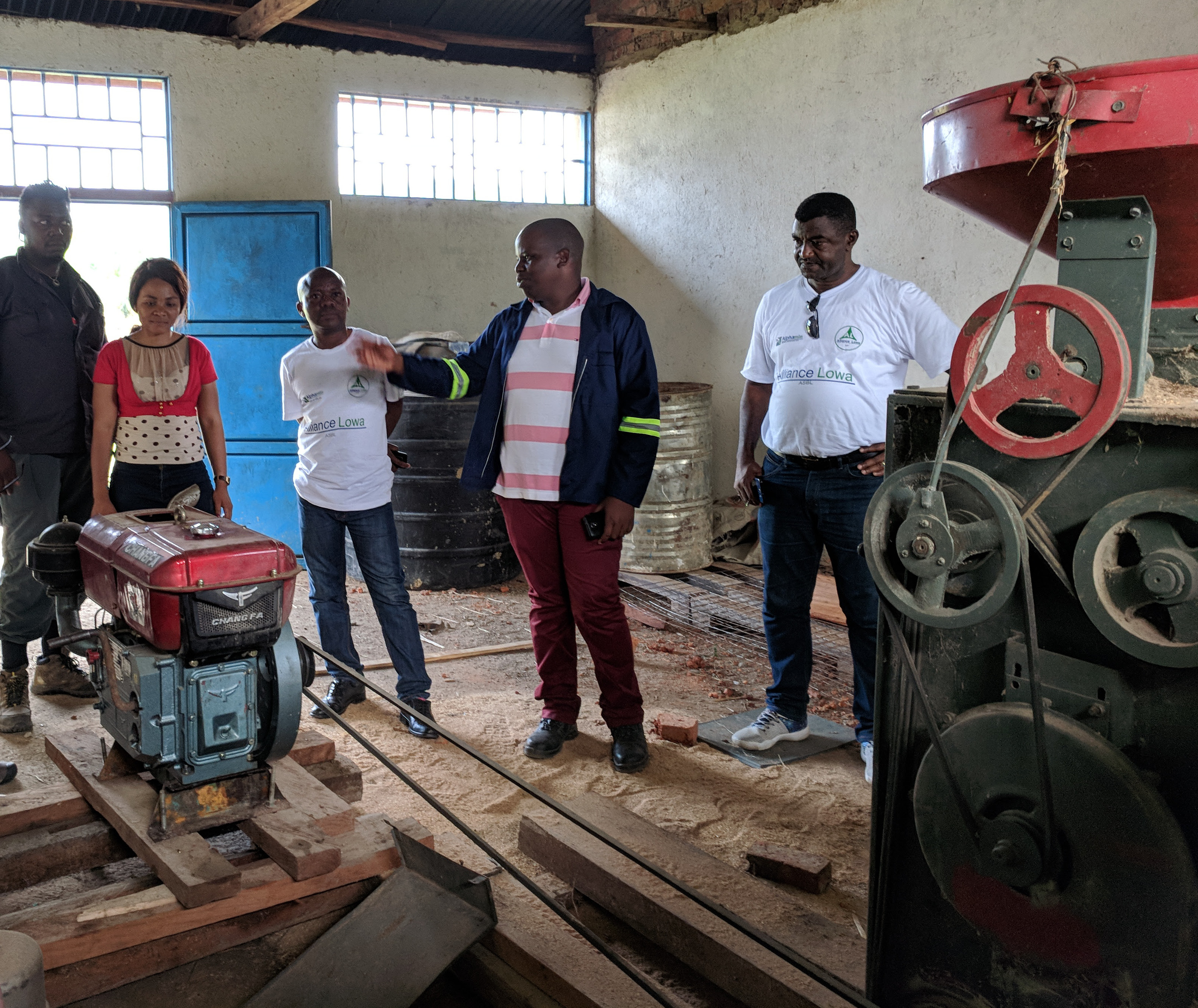 Five people gathered around a diesel-powered rice mill in the Democratic Republic of Congo.