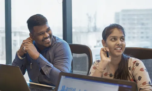 A woman wearing blue top in focus talking to another woman facing away from the camera.